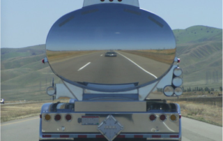 back of a stainless steel tractor trailer tank driving on the road