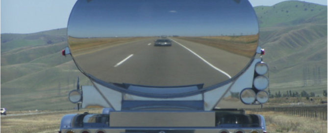 back of a stainless steel tractor trailer tank driving on the road