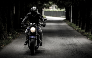 a motorcyclist wearing dark clothing driving down an alleyway