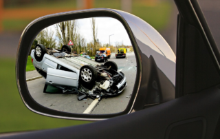 a car side mirror showing a car flipped on it's roof