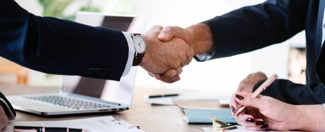 two men in suits shaking hands over a desk