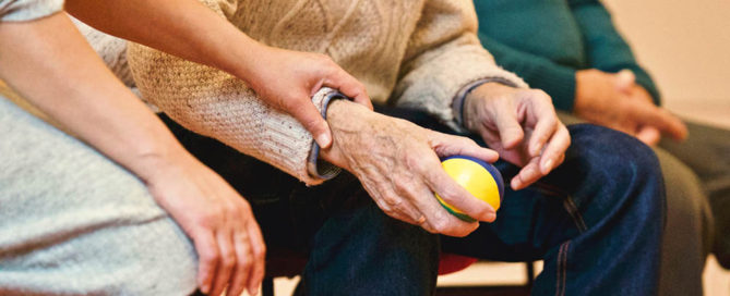 an old man sitting holding an exercise ball in one hand
