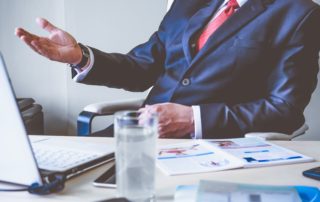 business man sitting behind a desk with laptop and materials on it