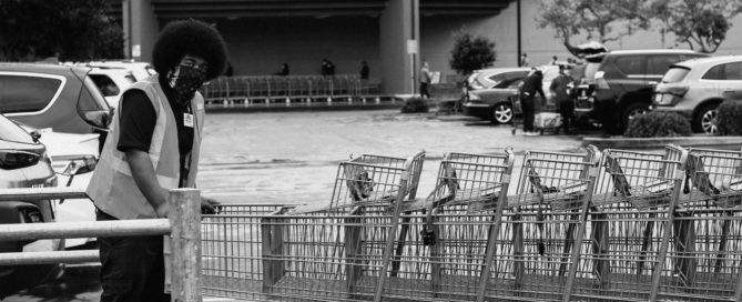 a man in a mask retrieving carts in a store parking lot